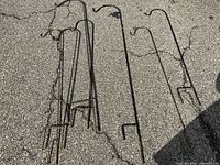 Seven metal outdoor shepherd's hooks laid out on pavement showing varying designs and rust wear.