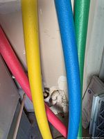 Four colorful pool noodles leaning against a wall, showing their colors and foam texture.