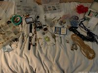 Full overview of assorted jewelry spread out including storage boxes, watches, and several necklaces and bracelets on fabric surface.