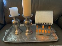 Front view of metal tray, two metal candle holders with pillar candles and Hallmark light-up house showing lit windows.