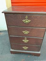 Side view of the wooden file cabinet showcasing four drawers with brass handles and the wood finish showing some wear and scratches.