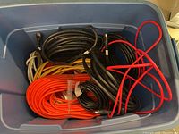 Photo of large Rubbermaid bin showing several coiled extension cords and HDMI cables inside the bin.