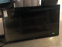 Photo of LG flatscreen TV with a black bezel and visible LG logo on bottom center. TV screen is off and reflective.