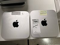 Top view of two silver Apple Mac mini desktops side by side showing Apple logos and identification labels