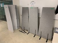 Four gray fabric divider panels on black metal stands against a wall