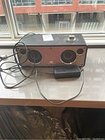 Front and side view of the black GGMM M3 wireless digital speaker with two speaker drivers, power adapter, and cables.