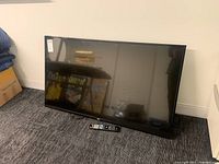 Front view of LG TV leaning on floor with remote placed below