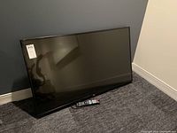Front view of LG flat-screen TV leaning against wall with remote in front on carpet.