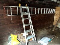 Aluminum extension ladder positioned horizontally on a wall with part of the step ladder leaning near bags and wood pieces on the ground.
