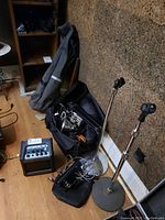 Photo showing two metal microphone stands, soft bags filled with cables and audio accessories, Passport mini amplifier on floor