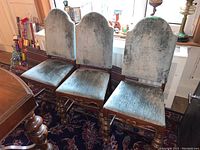 Front view of three side dining chairs with blue-gray velvet upholstery, turned wood legs and carved aprons.