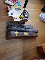 Violin cases and frequency tester equipment on wooden floor, showing condition and accessories.