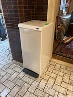 Side view of the tall white metal garbage can with black pedal