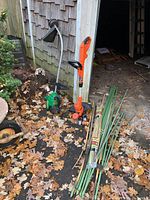 Full view of two lawn trimmers positioned outside next to a shed with scattered fall leaves and the plant stakes arranged next to them.