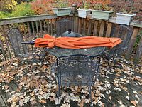 Overall view of metal mesh table, four chairs, umbrella folded across table