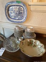 Photo showing the blue and white rectangular ceramic tray along with multiple floral patterned saucers, two matching teacups, clear glass plates, and the large floral serving bowl.