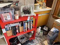 Wide view of the shelf with several small kitchen appliances, popover pan, and cookbooks below.
