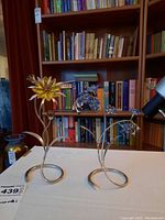 Both sculptures side by side on tabletop with bookshelf background