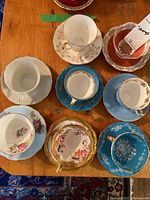 Top view of 8 porcelain teacups paired with matching saucers varying in floral designs and colors including blue, white, turquoise, and red with gold trim.