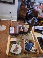 Photo of table showing vintage brass binoculars with brown leather case, brass telescope, Potter Teletone earphone in box, and three tin boxes including one with butterfly decoration.