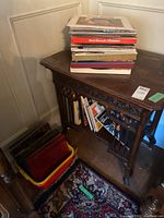 Stack of vinyl records on top of a carved wooden table and additional vinyl records in a plastic bin on the floor.