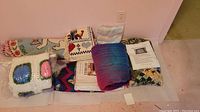 Photo of whole lot showing various folded blankets and quilts arranged against wall on floor, includes crocheted blanket in wrapping and woven cat design blanket