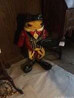 Large resin frog butler statue holding a black tray, dressed in red jacket with striped vest and red bow tie, positioned near wooden furniture.