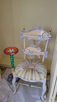 Front view of hand-painted chair with fish on backrest and striped cushioned seat next to a colorful wood stand.