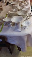 Table display of multiple white porcelain items including bowls, vases, soap trays, and serving dishes with gold detailing.