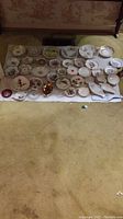 Full view of multiple plates, saucers, and small dishes arranged on a white cloth showing variety of floral and gold-trimmed china pieces