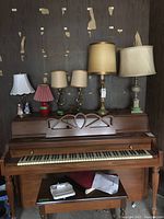 Six lamps arranged on and in front of a piano, showing variety of shades and bases.