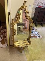 Full view of the ornate gold framed wall mirror with decorative shelf and surrounding environment.