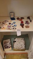 Photo showing two boxes of assorted necklaces on floor, and various pins and brooches laid out on shelf including Birks silver-tone brooch in box.