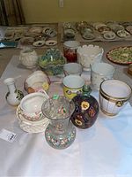 Overview photo showing multiple planter pots on a table, highlighting variety in colors, sizes, and designs including floral decorations and gold accents.