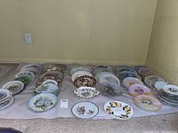 Overview of multiple collectible plates arranged on a cloth, showing a variety of floral and fruit designs.