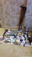 Wide view showing five walking canes leaning against wall and various decorative items spread on floor including suncatchers, animal figurines, hooks, candle holders, and candles.