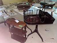 Photo showing three wooden pieces: a two-tier plant stand or small table, a pedestal table with a spindled gallery top, and a wall shelf in background.