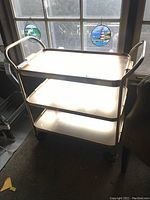 Front angled view of cart showing three shelves and wheels near window with decorative glass stickers.