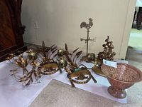 All items in lot displayed together including two pairs of gold-tone floral metal candle holders, copper-tone hammered metal bowl, and metal rooster figure weather vane stand.