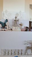 Various decorative wire and ceramic angels, butterfly figurine, bird figurine, ceramic heart, and busts on white shelves.