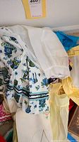 Pile of aprons showing white organza apron and patterned fabric apron with blue and green floral design