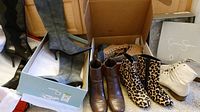 Four pairs of boots including tall gray heeled boots, brown leather ankle boots, leopard print boots, and light beige boots with box