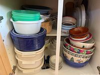 Photo of cupboard shelf showing stack of plastic storage containers in white, blue, and green colors along with some smaller bowls.