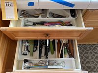 Top drawer fully open showing several compartments with silver-tone cutlery and black and blue floral handle pieces.