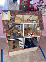 Full front view of wooden dollhouse showing three floors filled with various miniature wooden furniture and toys