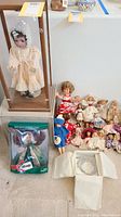 Overall lot view showing vintage baby doll in glass case, holiday doll in box, multiple small vintage dolls, and boxed tiara.
