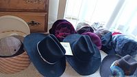 Several black wide-brimmed men's hats, some with decorative bands, and other colorful women's hats arranged together.