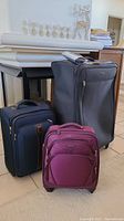 Photo showing all three pieces of luggage together: large dark suitcase, small purple Samsonite spinner suitcase, and medium navy blue rollerboard.