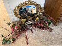 Full view of the oval gold composite framed mirror with dried flower arrangement displayed on floor.