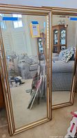Two full-length rectangular wall mirrors standing upright, showing their reflective surfaces and metal beaded gold frames.